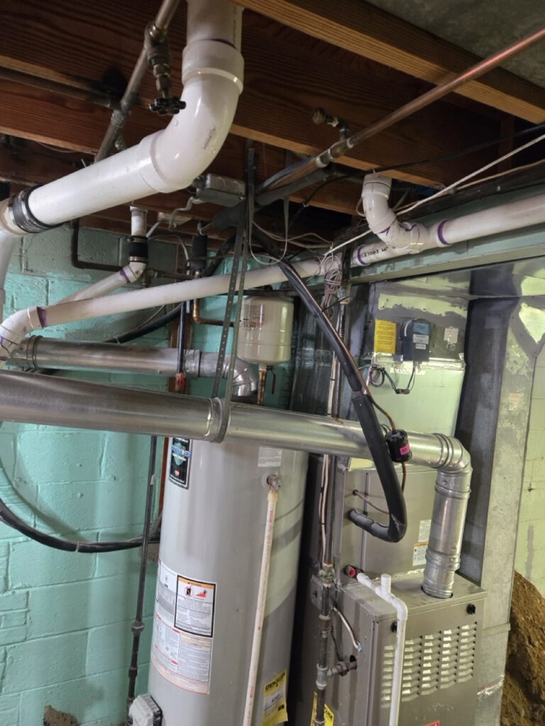 Home Messy residential basement plumbing with water heater, PVC drain lines, and HVAC connections needing repipe.