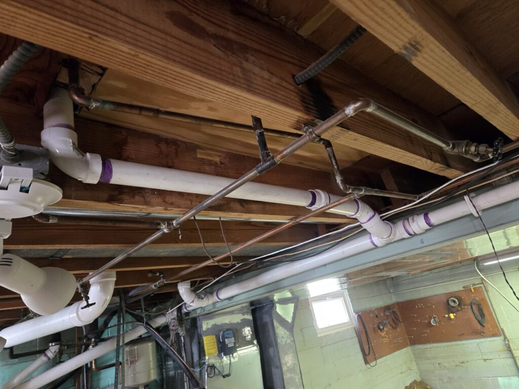 Home Messy basement plumbing with copper and PVC pipes and drain lines needing repiping in Gaithersburg, MD.