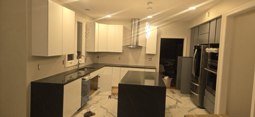 Gallery Newly remodeled kitchen with white cabinets, black countertops, and stainless steel range hood by Perfectum Construction & Plumbing.