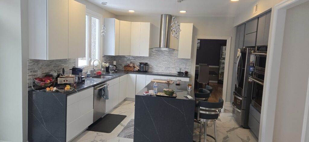 Gallery Completed kitchen remodel with modern white cabinetry, stainless steel appliances, and gray stone backsplash by Perfectum Construction & Plumbing.