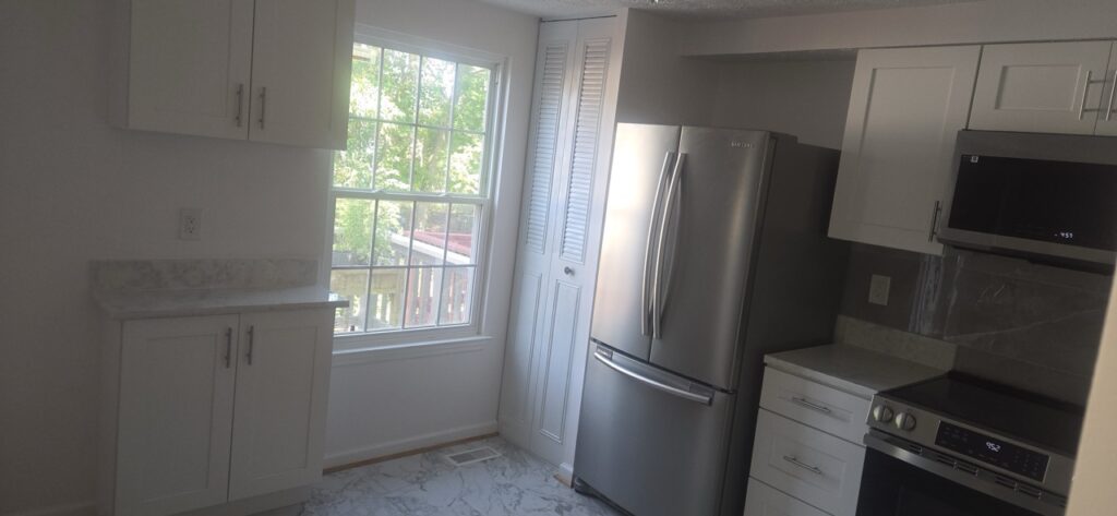 Gallery Completed kitchen remodel with white cabinetry, stainless steel appliances, and large window by Perfectum Construction & Plumbing.