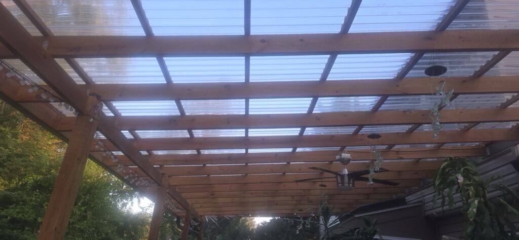 Gallery Wooden pergola with clear corrugated roofing and ceiling fan, showcasing Perfectum Construction & Plumbing remodeling project.