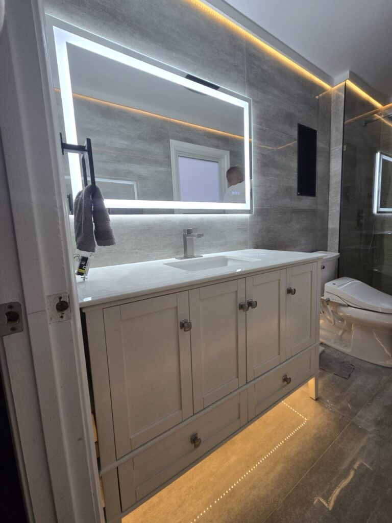 Gallery Modern bathroom remodel with vanity, lighted mirror, and tiled walls by Perfectum Construction & Plumbing.