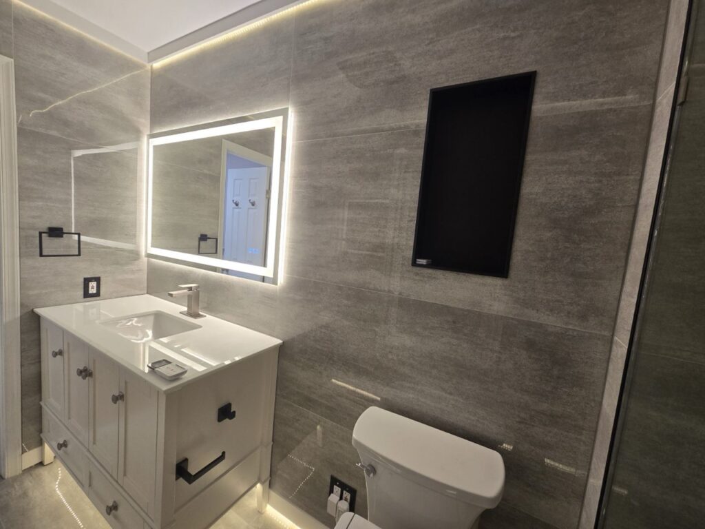 Gallery Newly remodeled bathroom with gray tile, vanity, and modern lighting by Perfectum Construction & Plumbing.